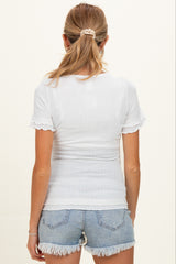 woman wearing a white short sleeve maternity top with a textured pattern and ruffle detailing, paired with denim shorts