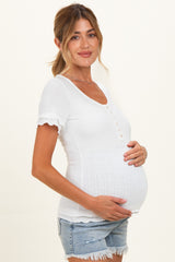 woman wearing a white short sleeve maternity top with button details and holding her baby bump