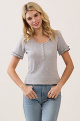 woman wearing a light gray short sleeve henley top with button details and ruffled cuffs, paired with blue jeans