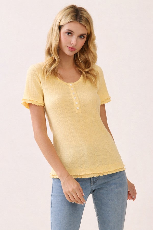 woman wearing a yellow short sleeve ribbed top with button details and frayed hem, paired with blue jeans