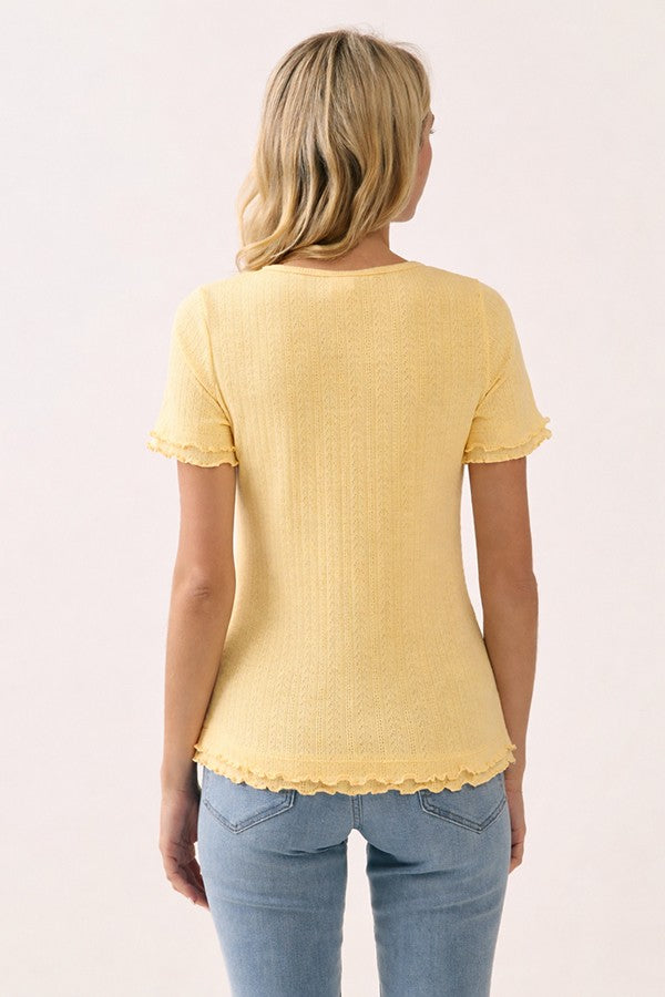 woman wearing a yellow short sleeve top with textured details and ruffle hem, paired with light blue jeans