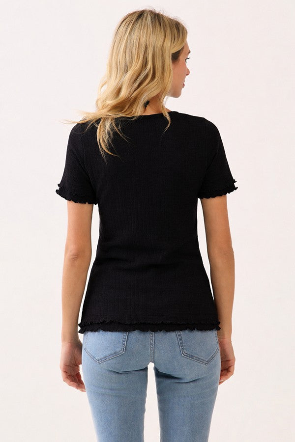 woman wearing a black ribbed short sleeve top with ruffle trim, paired with light blue jeans, shown from the back