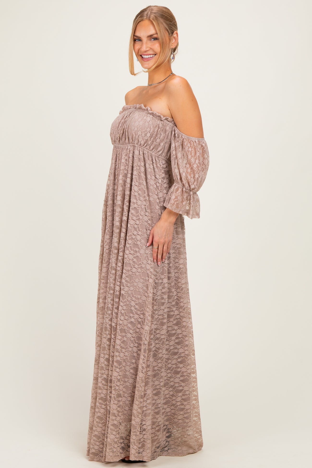 woman wearing a taupe off-the-shoulder maxi dress with sheer sleeves and a flowing silhouette