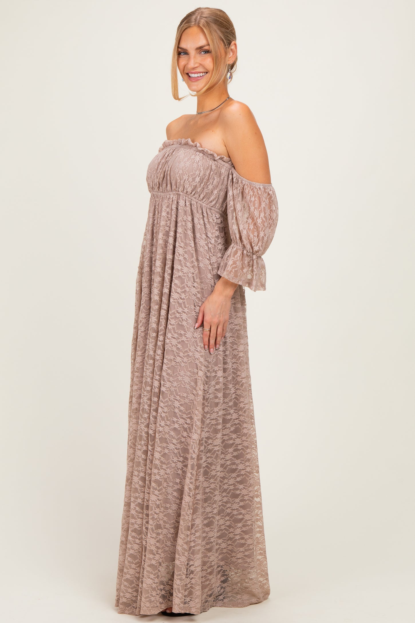 woman wearing a taupe off-the-shoulder maxi dress with sheer sleeves and a flowing silhouette