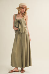 woman wearing a sage green two-piece set with a bow detail and wide-leg pants, paired with a straw hat and sandals