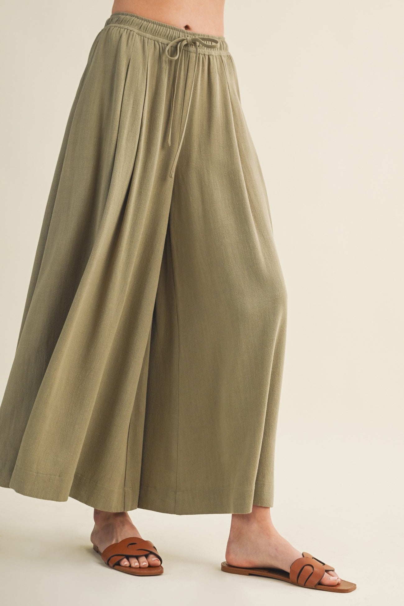 woman wearing olive green wide-leg pants with a drawstring waist and brown slip-on sandals