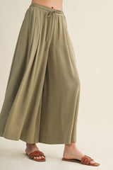 woman wearing olive green wide-leg pants with a drawstring waist and brown slip-on sandals