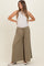 woman wearing olive green maternity wide-leg pants with a drawstring waist and a fitted white tank top, smiling with hands on hips