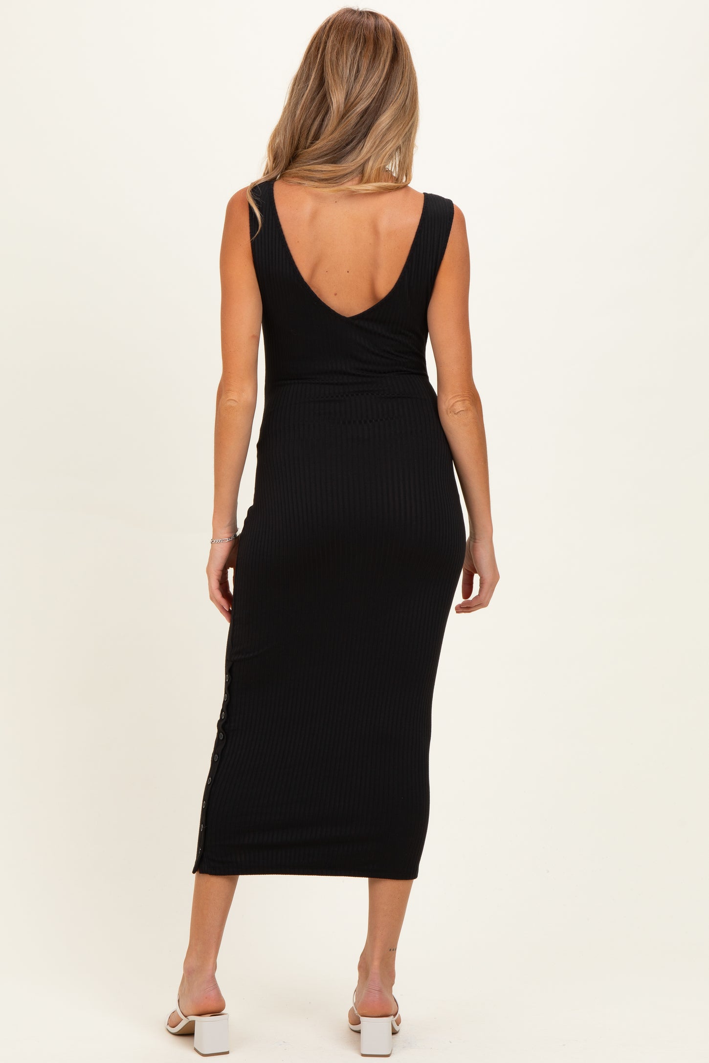 woman wearing a black ribbed maternity dress with a deep v-back and side button detail, highlighting a baby bump