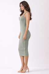 woman wearing a fitted olive green ribbed midi dress with thin straps and a side slit, standing in profile
