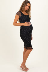 woman wearing a black maternity dress with cap sleeves and floral print, holding her baby bump