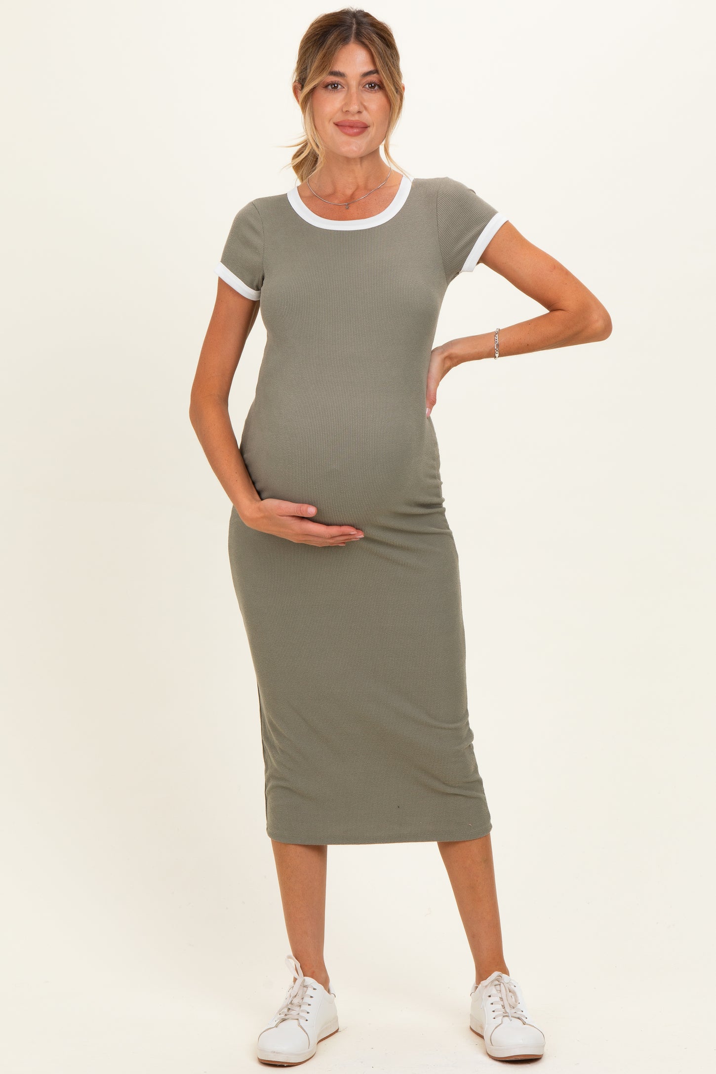 woman wearing a fitted olive green maternity dress with white trim and holding her baby bump