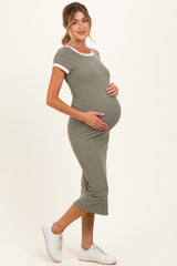 woman wearing a light olive green ribbed maternity dress with white trim, showing her baby bump and smiling