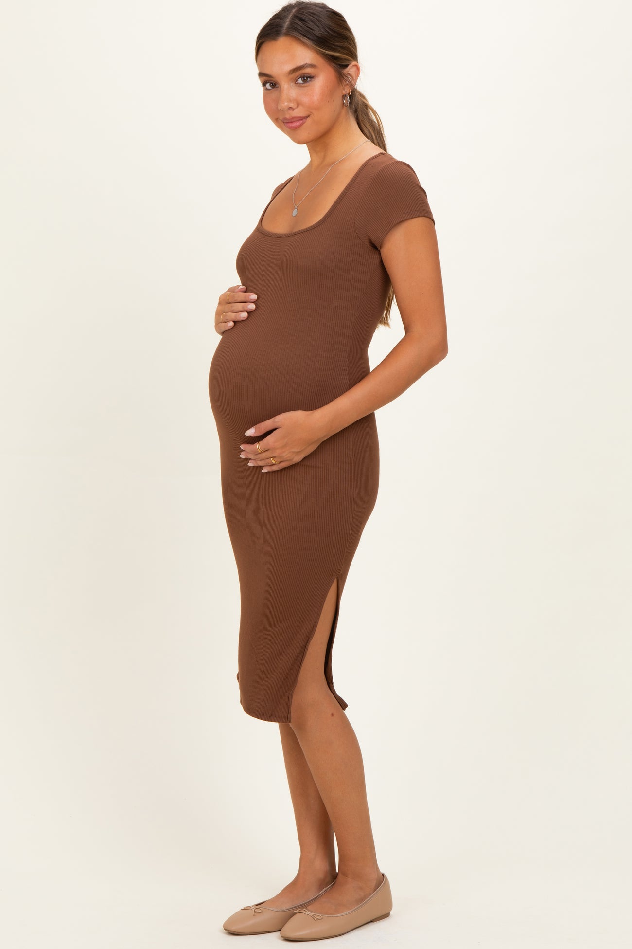 woman wearing a brown ribbed maternity dress with short sleeves and side slits, highlighting her baby bump