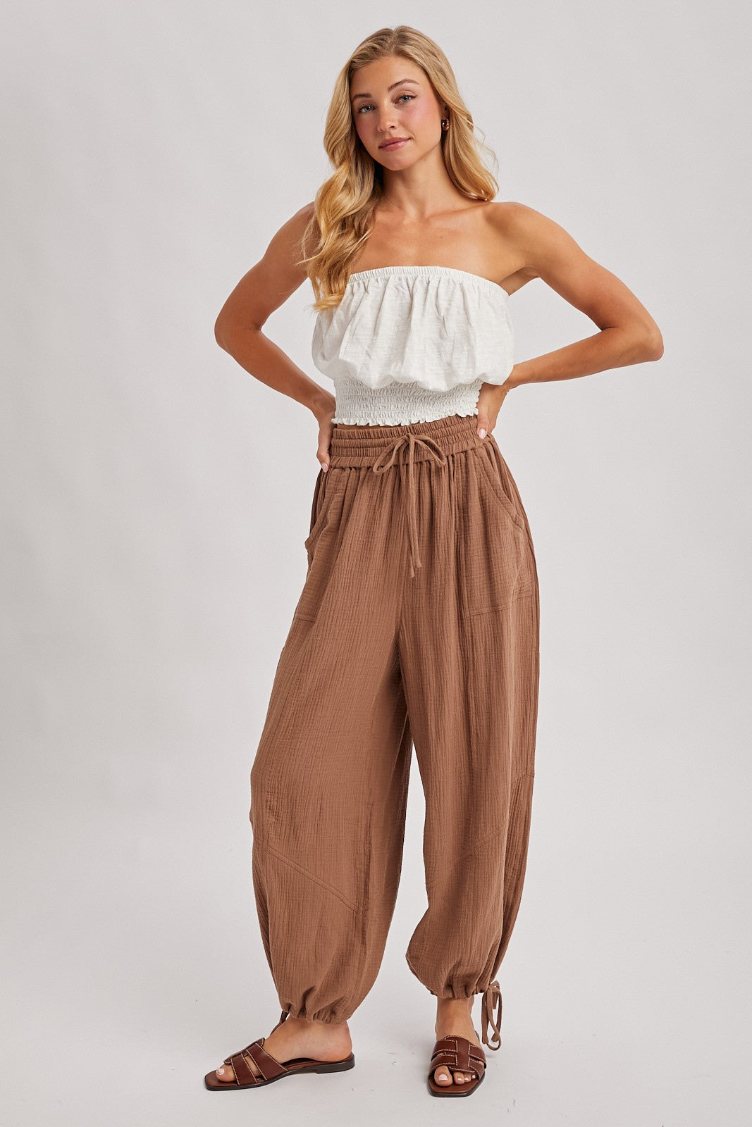woman wearing a white smocked strapless top and brown loose fit drawstring pants