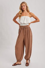 woman wearing a white smocked strapless top and brown loose fit drawstring pants