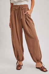 woman wearing brown loose-fitting lounge pants with pockets and drawstring waist, paired with brown slide sandals