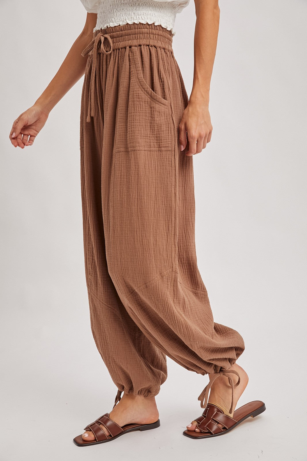 woman wearing brown textured high-waisted pants with side pockets and elastic cuffs, styled with brown sandals