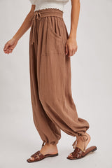 woman wearing brown textured high-waisted pants with side pockets and elastic cuffs, styled with brown sandals