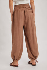 woman wearing light brown relaxed fit pants with an elastic waistband and drawstring cuffs, seen from the back