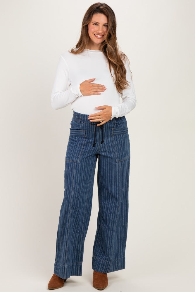 woman wearing a white long sleeve maternity top and blue striped wide-leg maternity pants, holding her baby bump