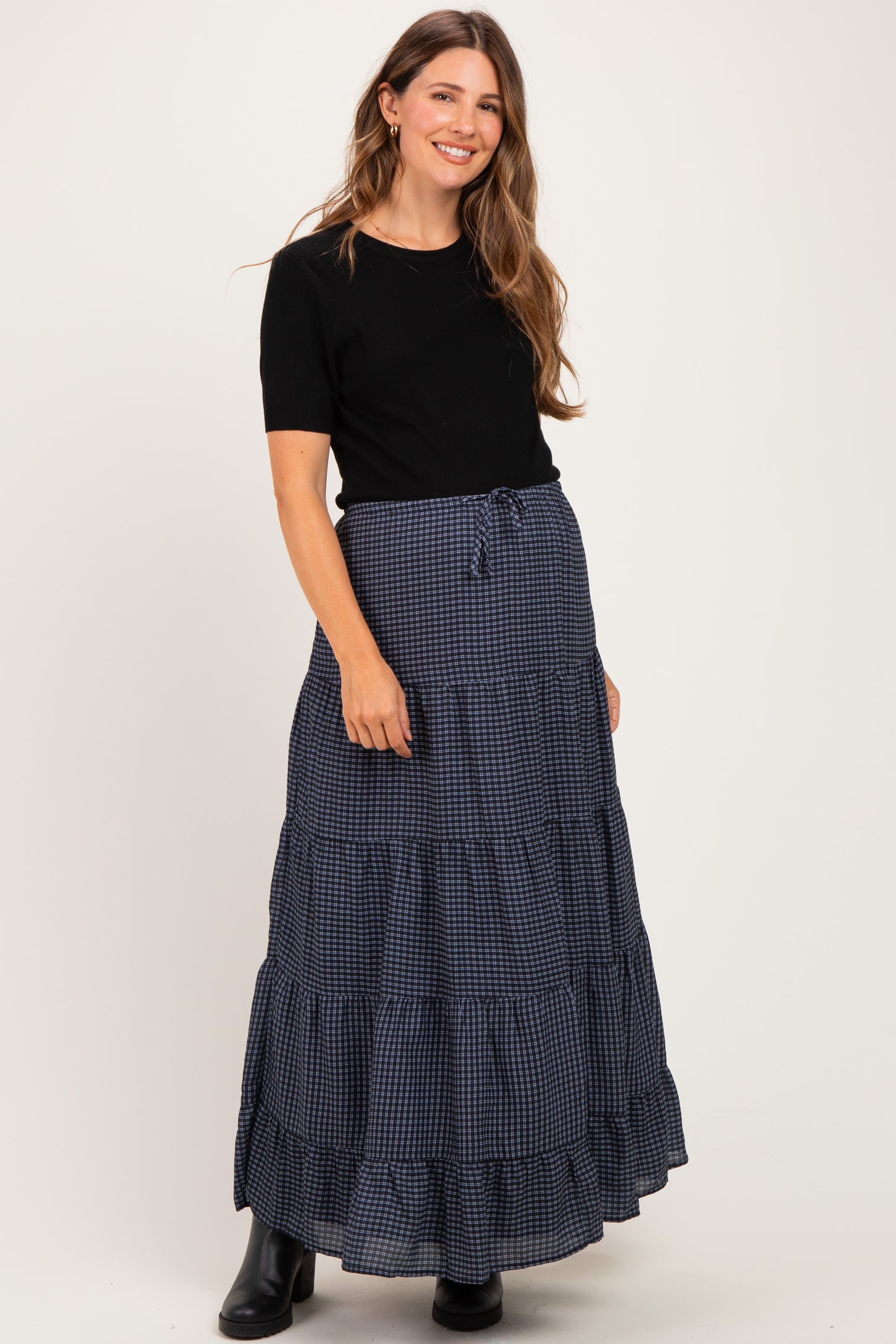 woman wearing a black short sleeve top and a navy and white checkered maternity maxi skirt with tiers