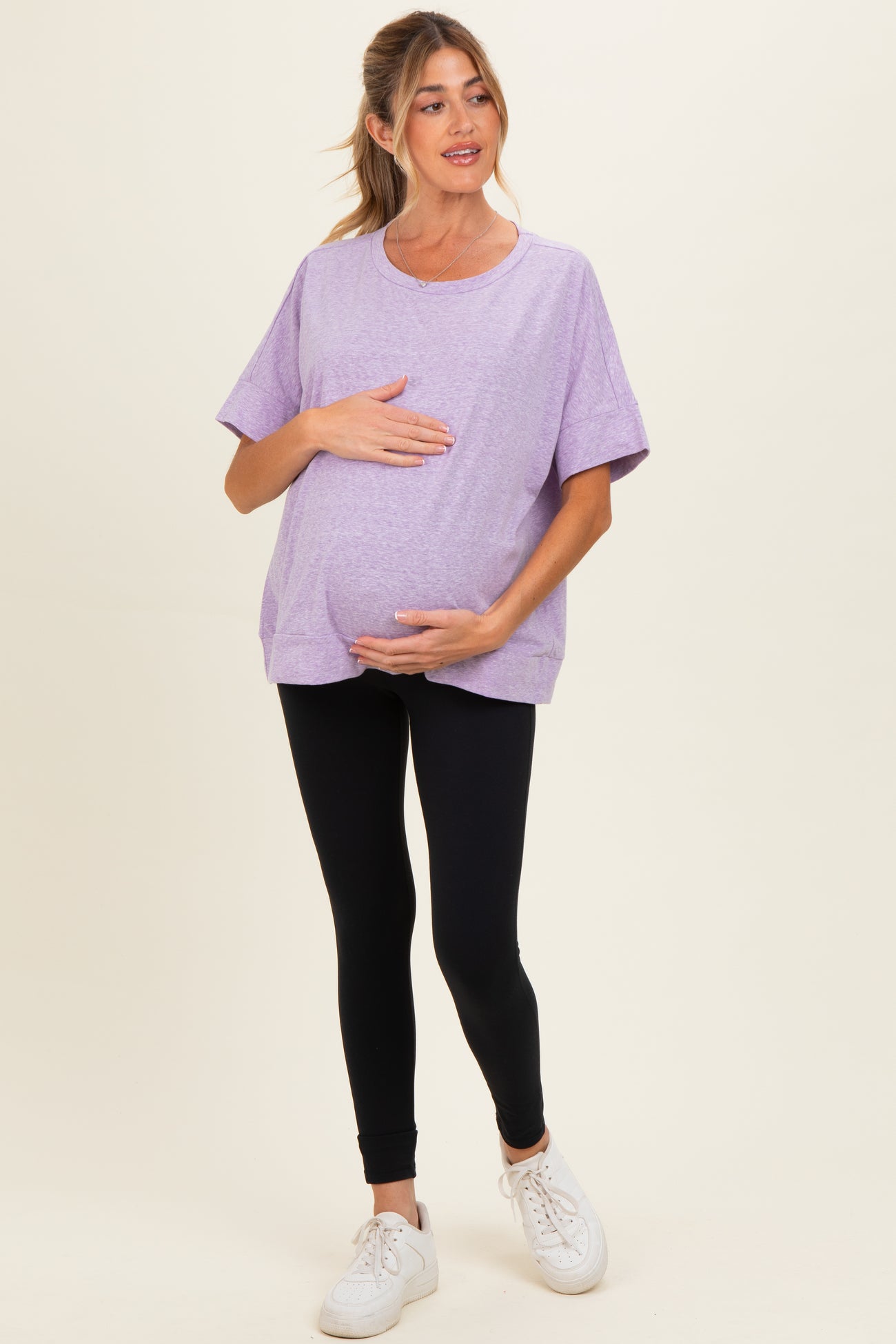 woman wearing a purple oversized maternity t-shirt and black leggings, holding her baby bump