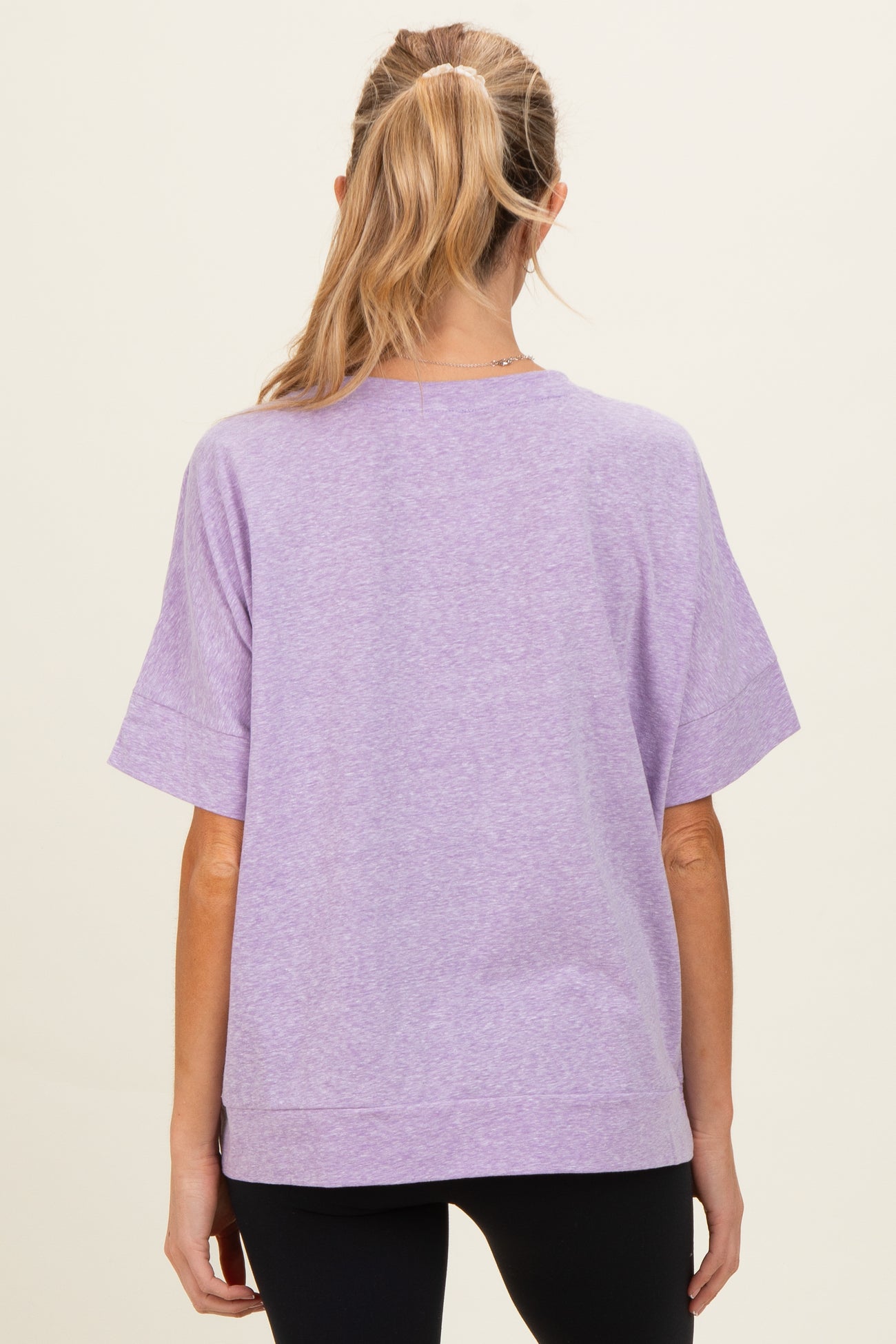 woman wearing a lavender short sleeve maternity top, viewed from the back with a relaxed fit and side slits