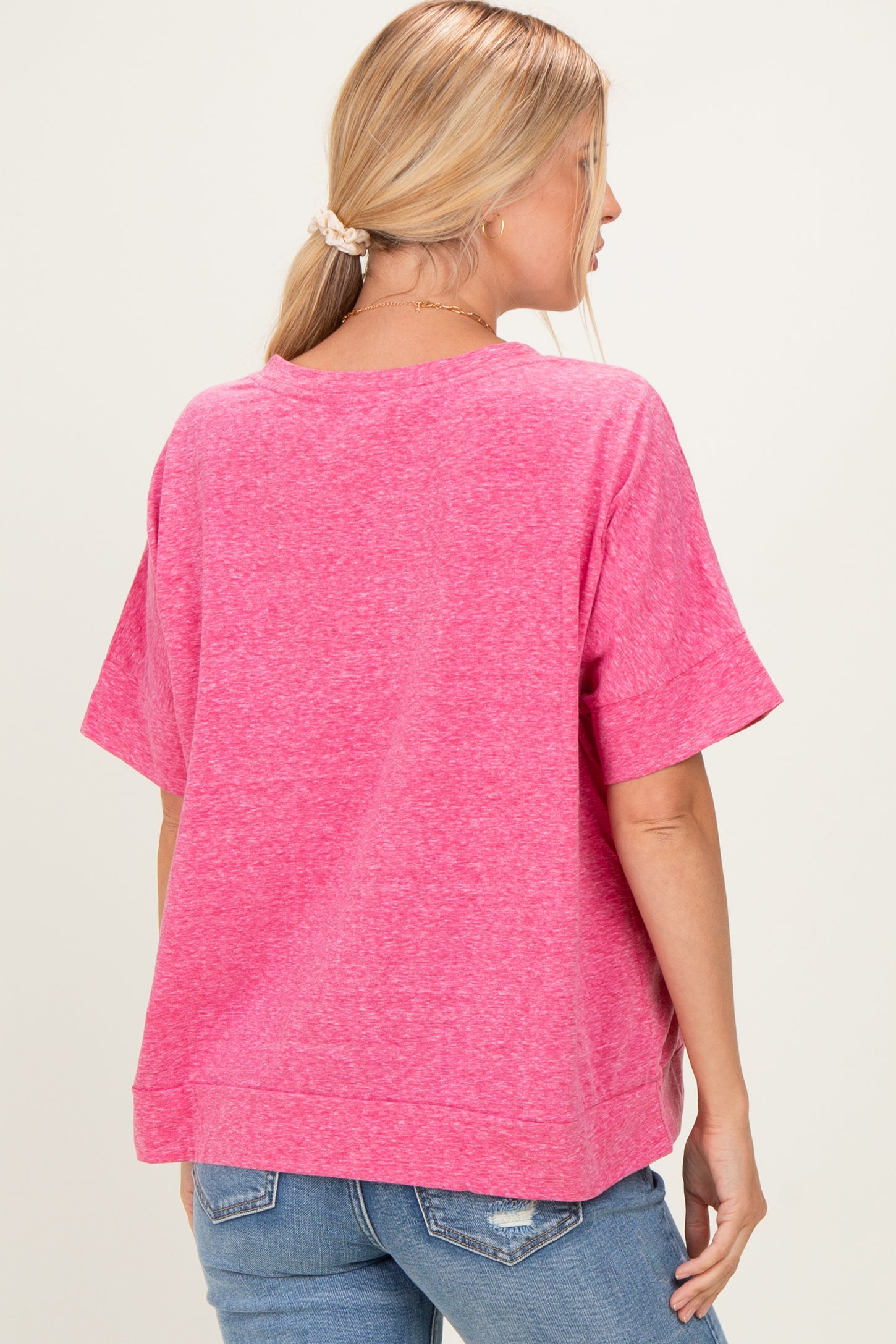 woman wearing a pink oversized short sleeve shirt with a relaxed fit and back seam detail, paired with blue jeans