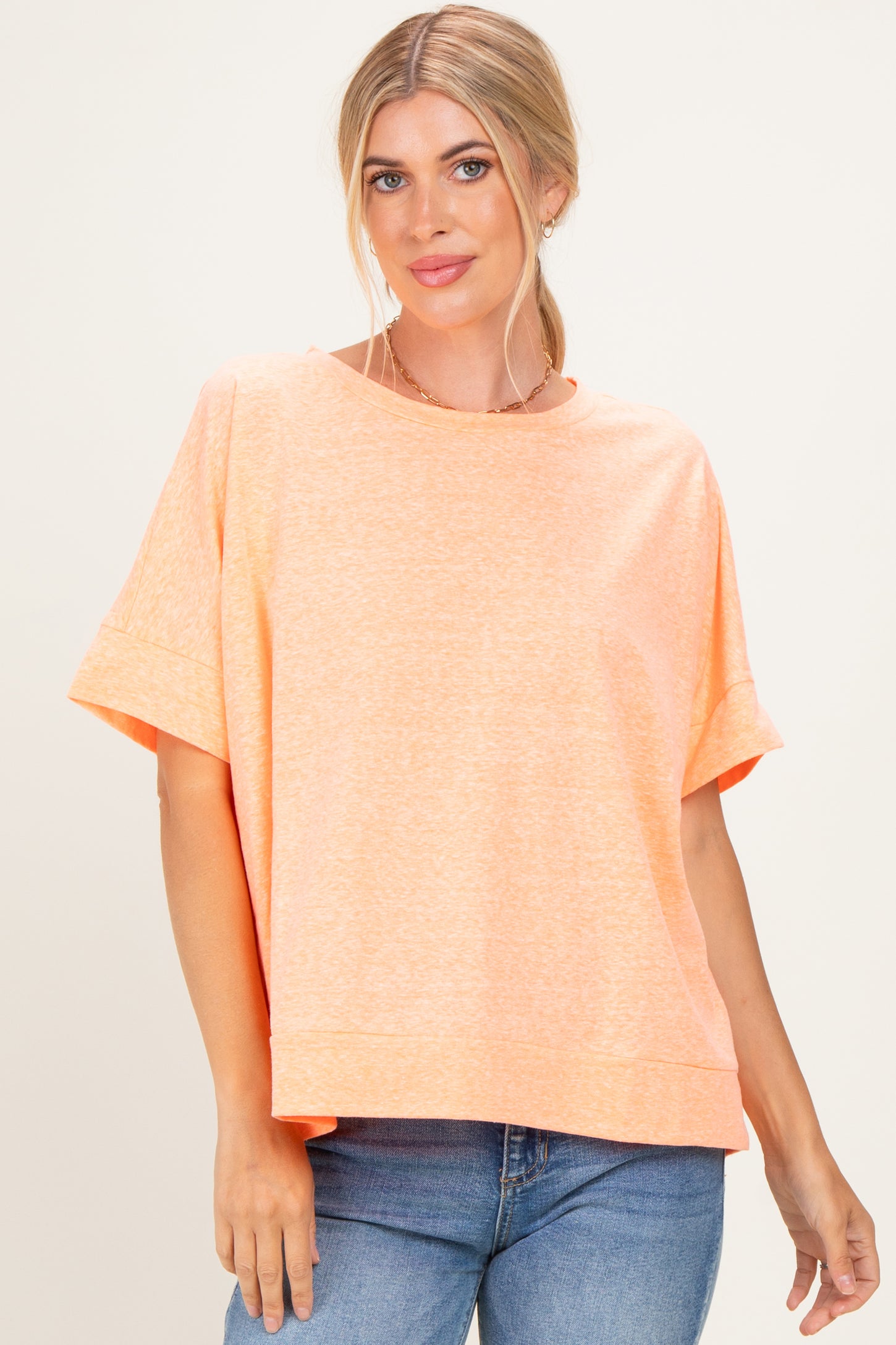 woman wearing an oversized light orange short sleeve top with a rounded neckline and relaxed fit paired with blue jeans