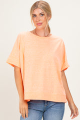 woman wearing an oversized light orange short sleeve top with a rounded neckline and relaxed fit paired with blue jeans