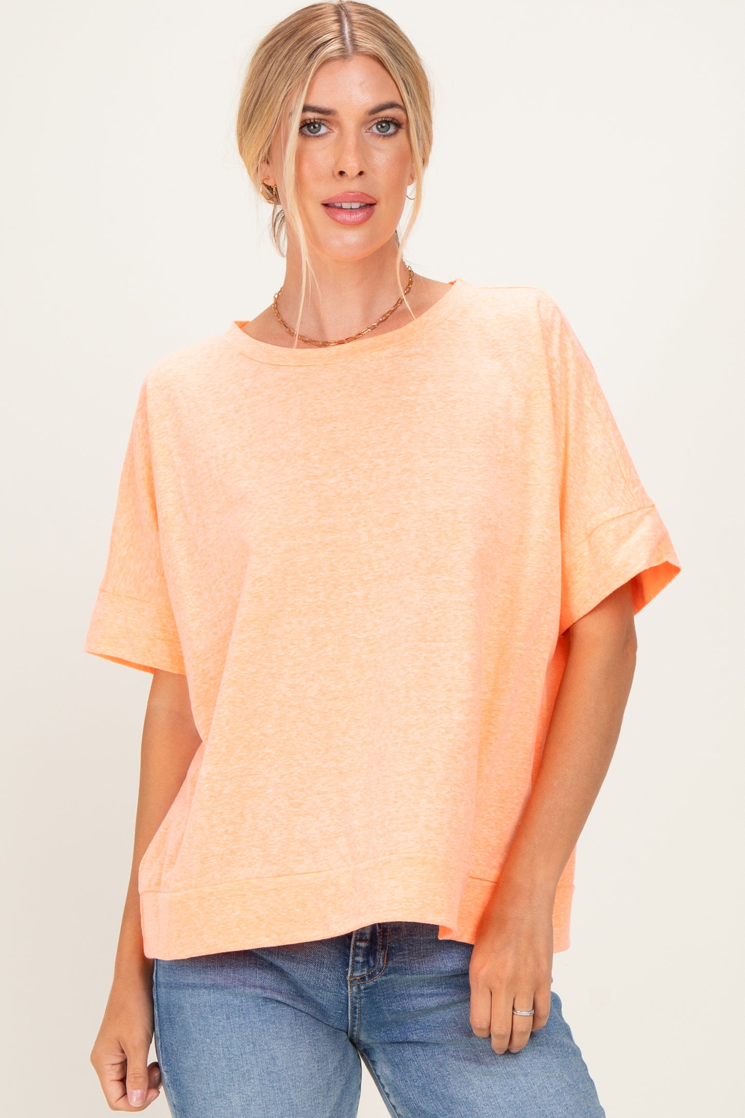 woman wearing an oversized light orange t-shirt with short sleeves and a relaxed fit, paired with blue jeans