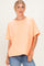 woman wearing an oversized light orange t-shirt with short sleeves and a relaxed fit, paired with blue jeans