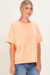 woman wearing a coral short sleeve oversized top with a rounded neckline and relaxed fit, paired with blue jeans