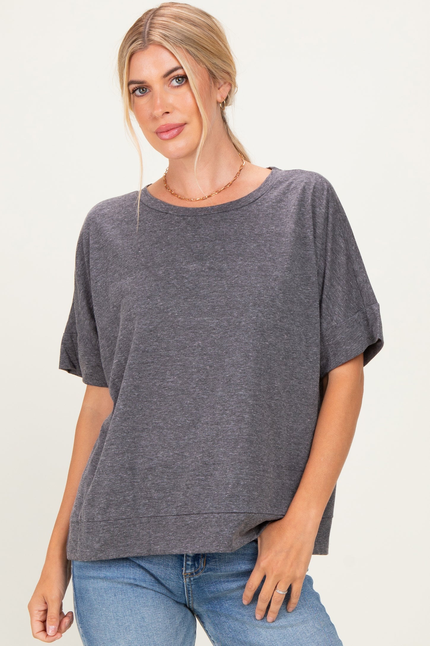 woman wearing a gray oversized short sleeve top with a relaxed fit and rolled sleeves, paired with blue jeans