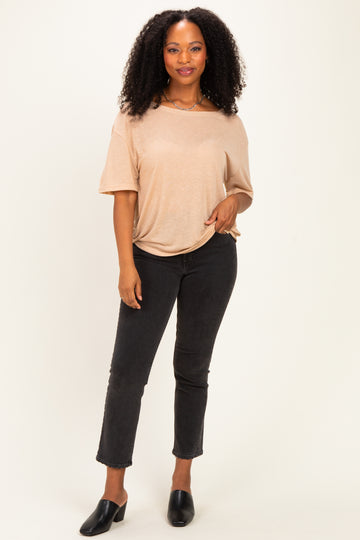 woman wearing a beige short sleeve top and black slim fit jeans, standing with hand on hip