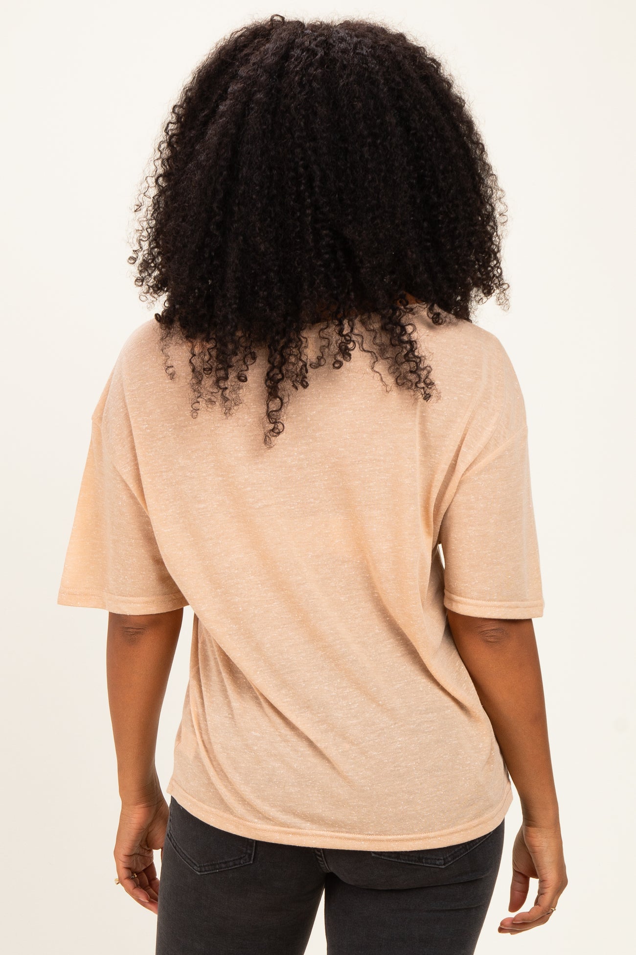 woman wearing a light peach short sleeve top, viewed from the back, paired with dark jeans