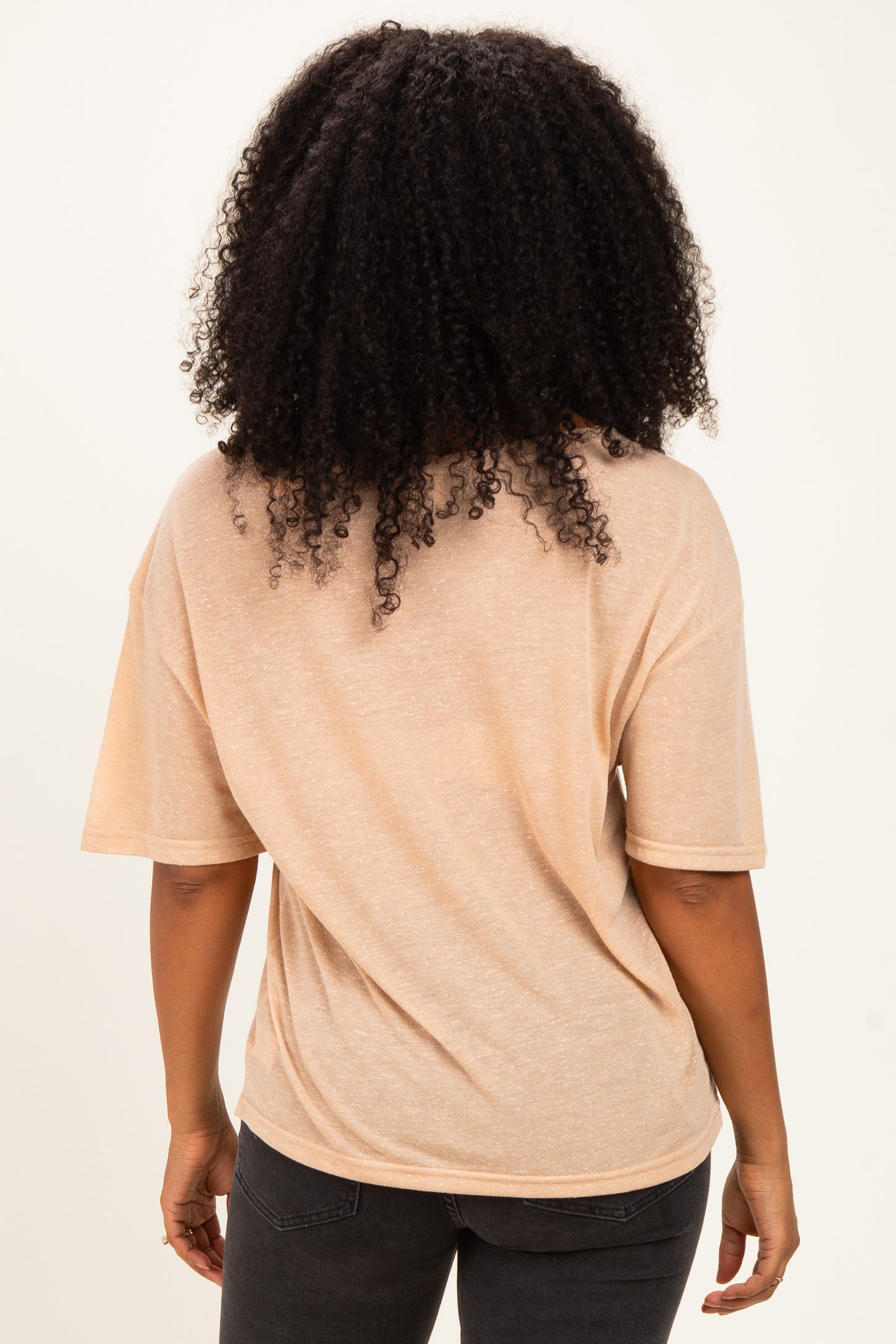 woman wearing a light peach short sleeve top, viewed from the back, paired with dark jeans
