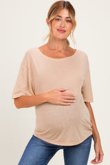 woman wearing a beige short sleeve maternity top and holding her baby bump, paired with blue jeans