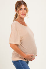 woman wearing a beige short sleeve maternity top and holding her baby bump