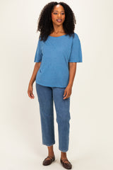 woman wearing a blue short sleeve top and high-waisted jeans, standing with a relaxed pose