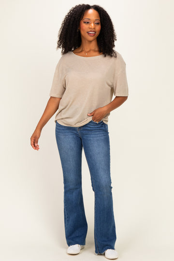 woman wearing a beige short sleeve top and blue flared jeans, standing and smiling against a neutral background