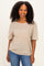 woman wearing a light brown oversized t-shirt with short sleeves and curly hair, posing and smiling