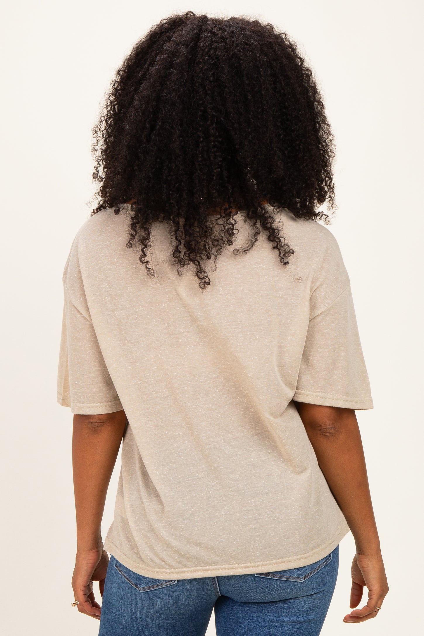 woman wearing a beige oversized t-shirt with short sleeves, viewed from the back, paired with denim jeans