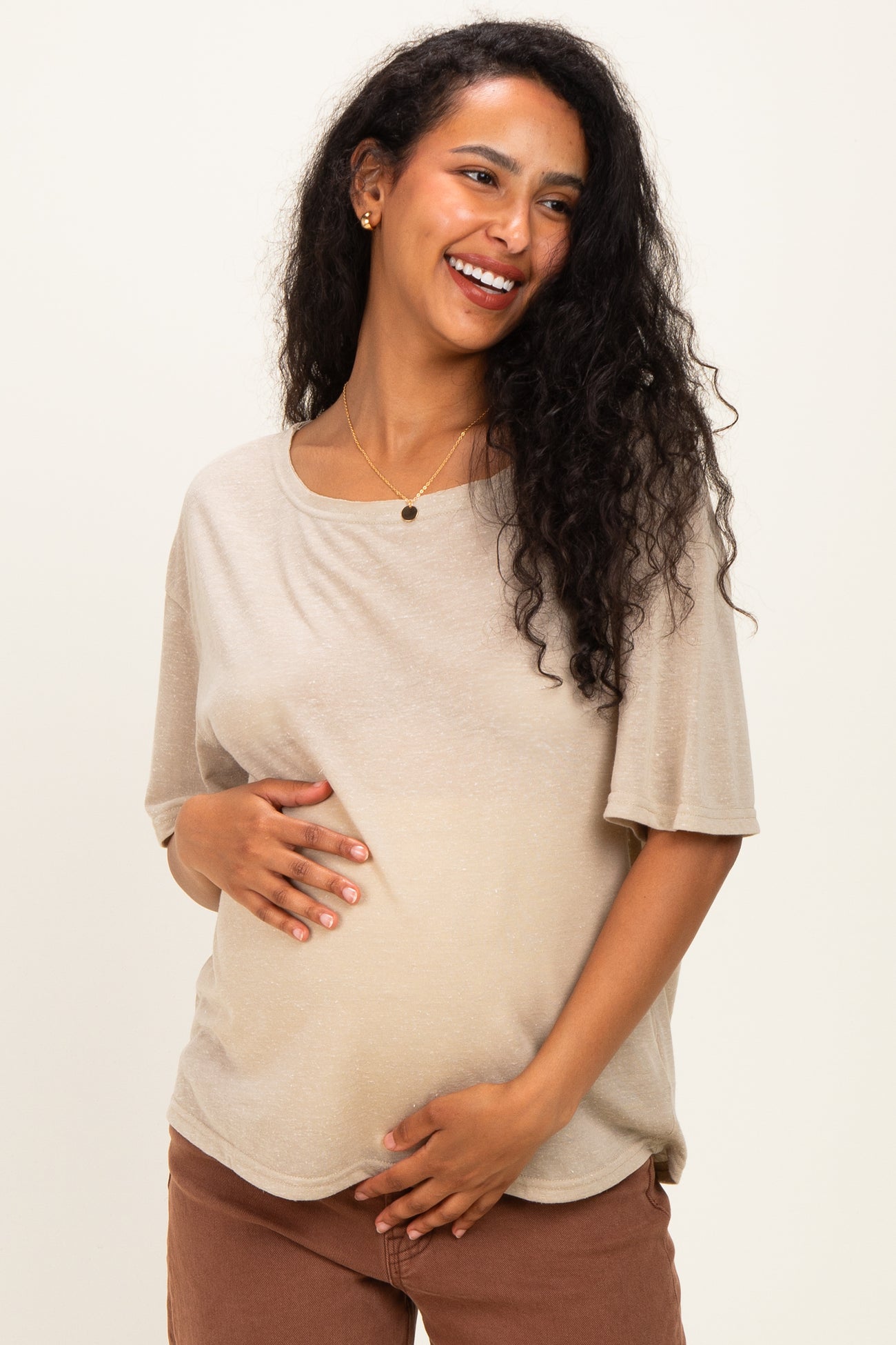 woman wearing a soft beige maternity top, smiling and gently holding her baby bump