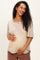 woman wearing a soft beige maternity top, smiling and gently holding her baby bump