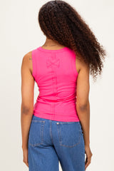 woman wearing a fuchsia sleeveless top with a bow detail on the back and blue high-waisted jeans