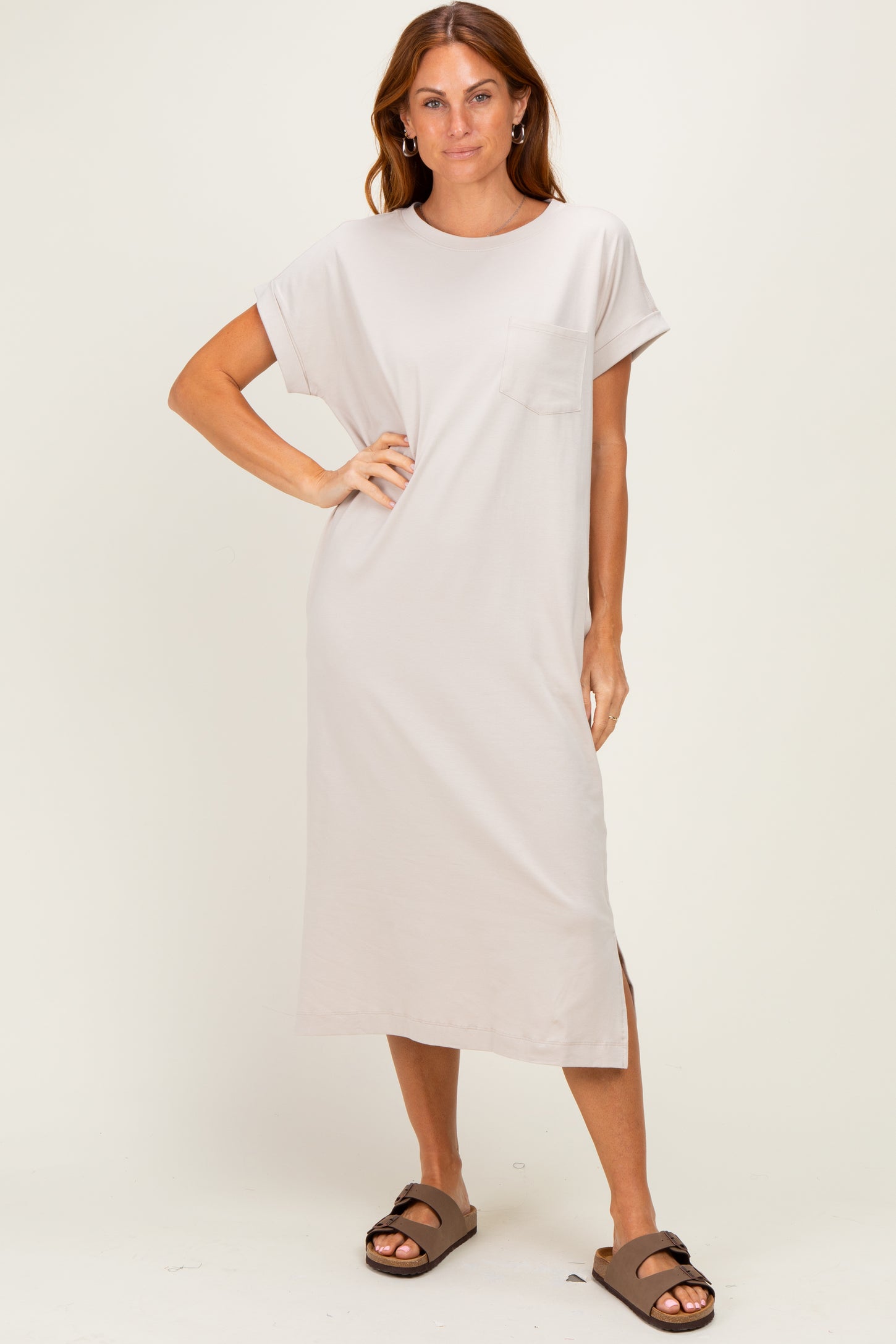 woman wearing a light beige short sleeve maxi dress with a pocket and side slit, paired with brown slides