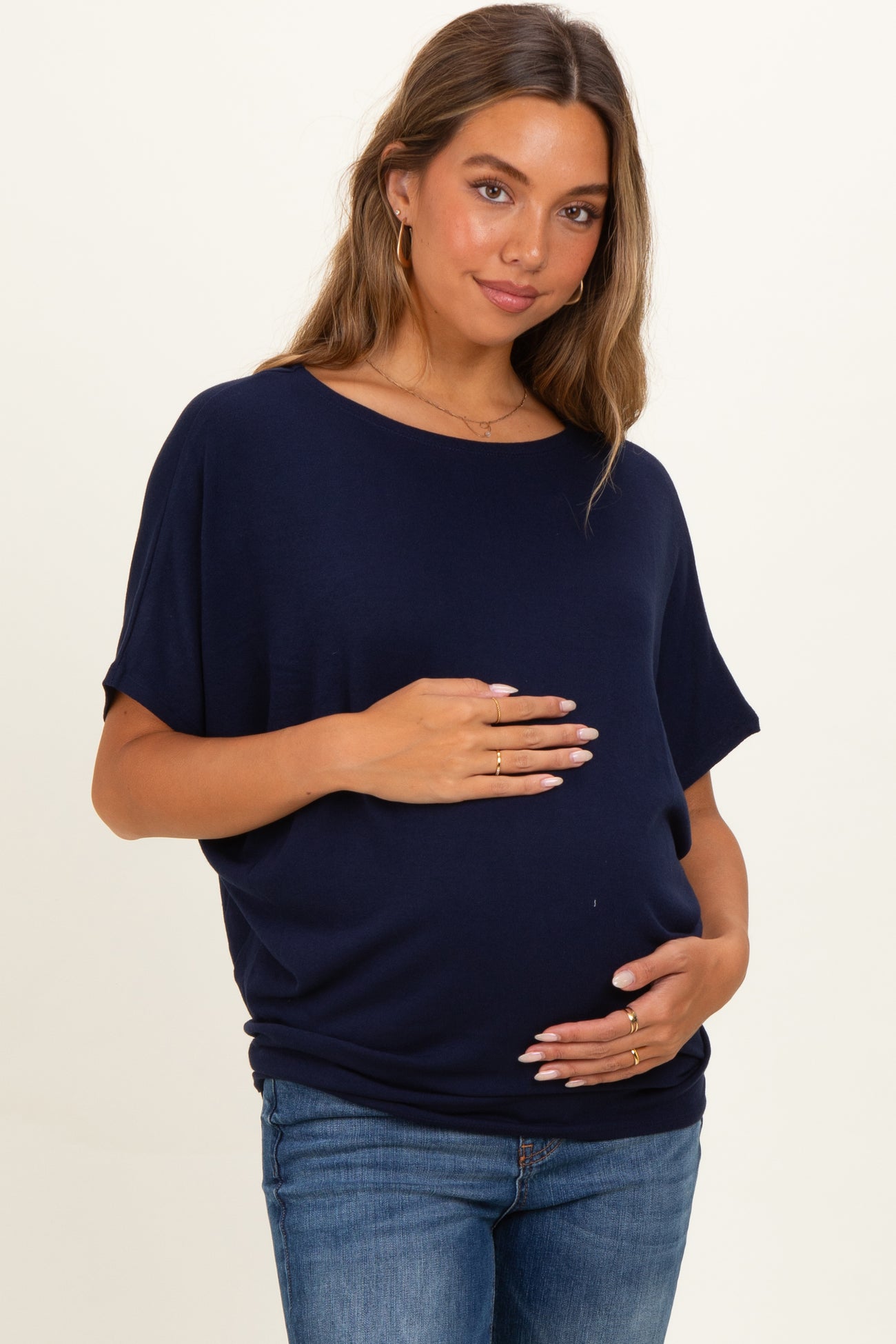 woman wearing a navy blue maternity top and holding her baby bump, paired with blue jeans