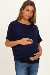 woman wearing a navy blue maternity top and holding her baby bump, paired with blue jeans